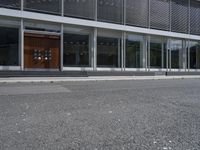 two people walking down the side walk towards a modern building with a large open glass front entrance