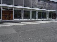 two people walking down the side walk towards a modern building with a large open glass front entrance