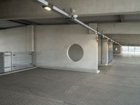 a parking garage that has cement floors and round holes on the wall and floor in front of door, ceiling