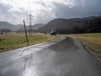 a country road lined with utility lines and power lines as a backdrop of mountains is shown on the horizon