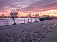 a person sitting on a bench looking at the ocean at sunset near a dock with a lot of boats