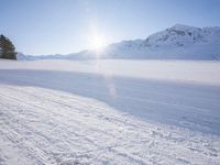 a man on skis going down a snowy hill with trees behind him and a sun shining through the clouds