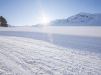 a man on skis going down a snowy hill with trees behind him and a sun shining through the clouds