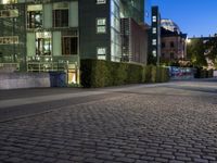 an empty square next to buildings at night, with a blue sky above the street