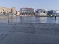 the empty street is beside an industrial building overlooking a large body of water with many buildings