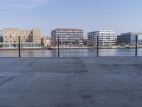 the empty street is beside an industrial building overlooking a large body of water with many buildings