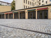 a building with lots of doors next to a sidewalk next to a brick walkway and sidewalk