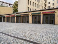 a building with lots of doors next to a sidewalk next to a brick walkway and sidewalk