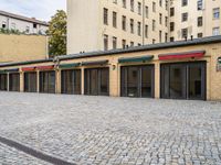 a building with lots of doors next to a sidewalk next to a brick walkway and sidewalk