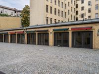 a building with lots of doors next to a sidewalk next to a brick walkway and sidewalk