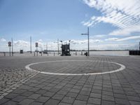 circular white and black stone walkway with building in the background on water's edge