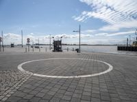 circular white and black stone walkway with building in the background on water's edge