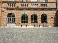 two benches near a brick building that has windows on both sides of the building and has stone floors