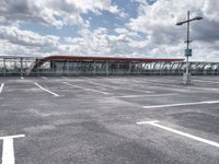 parking lot with clouds overhead and a pedestrian crossing sign to the left of it, next to an overhang