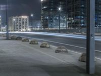 the empty city road is empty by the tall building in the background at night with light streaking on the buildings