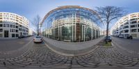 a mirror image of cars outside a glass building on the street and a building to the right side