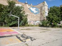 a basketball court with graffiti all over it with a person on a bike and buildings with trees in the background