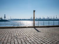 the view of a brick sidewalk in front of a body of water with a few industrial area behind it