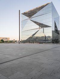 the exterior of a large building with lots of glass on top of it and people walking about it