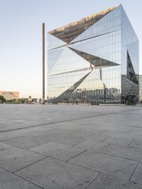 the exterior of a large building with lots of glass on top of it and people walking about it