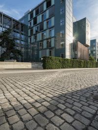 two people walking along a brick road next to tall buildings on a sunny day that looks like an office building