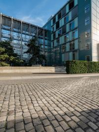 two people walking along a brick road next to tall buildings on a sunny day that looks like an office building