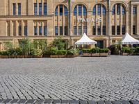 a large stone parking lot in front of a tall building that has some people underneath umbrellas