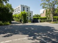 a white house with green plants and bushes in the yard with the driveway paved with cement