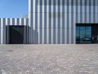 a brick walkway leading to a metal door in front of a building with a wall covered in vertical stripes