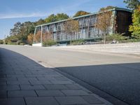 an industrial building with a big green roof and stairs next to trees on the side walk