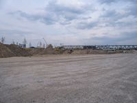 a dump truck is sitting in a dirt field near a bridge and building site,