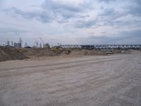 a dump truck is sitting in a dirt field near a bridge and building site,