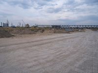 a dump truck is sitting in a dirt field near a bridge and building site,