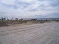 a dump truck is sitting in a dirt field near a bridge and building site,