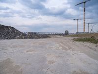 construction is taking place on a big lot of rubble near a railroad track and bridge