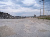 construction is taking place on a big lot of rubble near a railroad track and bridge