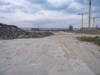 construction is taking place on a big lot of rubble near a railroad track and bridge