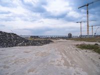 construction is taking place on a big lot of rubble near a railroad track and bridge