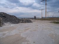 construction is taking place on a big lot of rubble near a railroad track and bridge