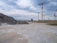 construction is taking place on a big lot of rubble near a railroad track and bridge