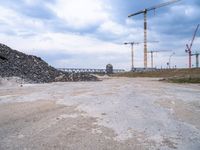 construction is taking place on a big lot of rubble near a railroad track and bridge