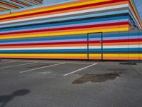 an empty parking lot painted brightly stripes on the wall of the building and sky as well as stones