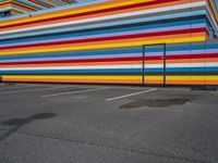 an empty parking lot painted brightly stripes on the wall of the building and sky as well as stones