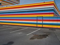 an empty parking lot painted brightly stripes on the wall of the building and sky as well as stones