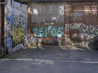 an empty garage filled with graffiti on a brick wall near a parking area with bicycles and a bike