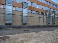 a side walk near a large building with two people walking on the sidewalk behind it