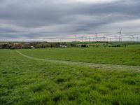 a green field with windmills in the distance under a cloudy sky with white clouds