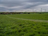 a green field with windmills in the distance under a cloudy sky with white clouds