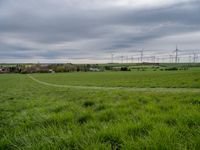 a green field with windmills in the distance under a cloudy sky with white clouds