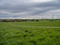 a green field with windmills in the distance under a cloudy sky with white clouds